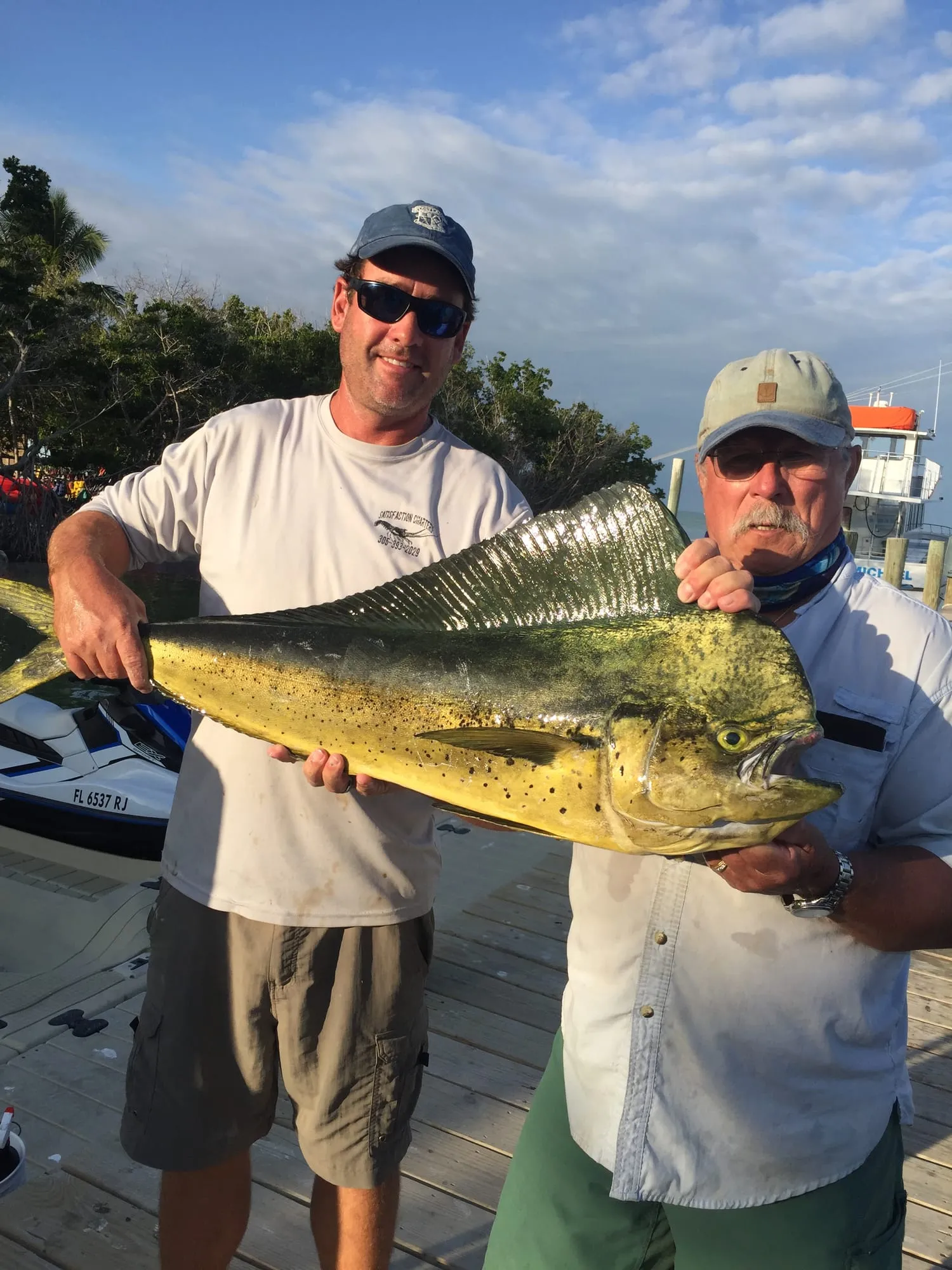 Two anglers holding a big mahi-mahi at the dock